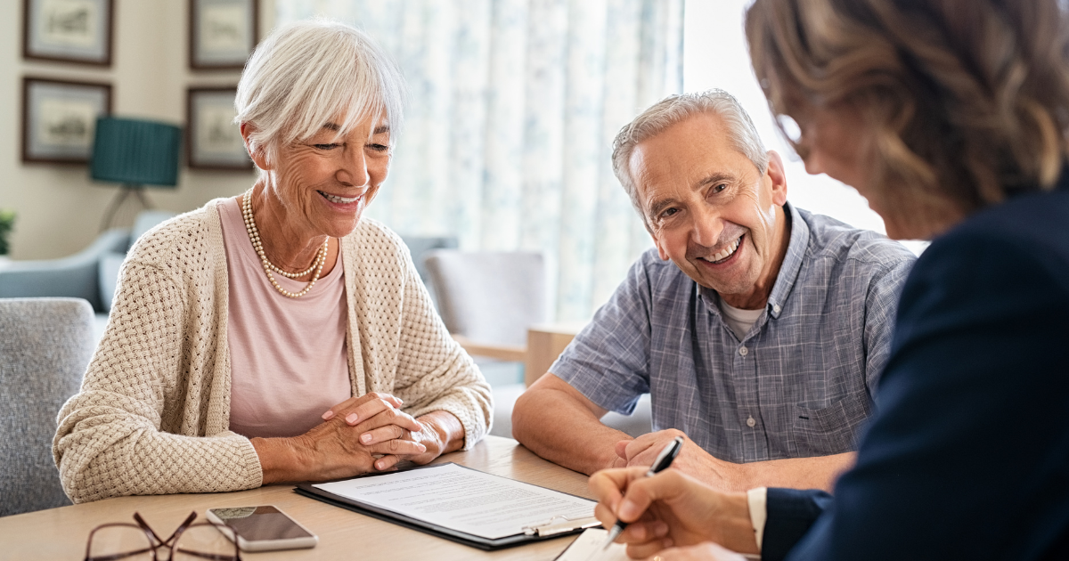 A smiling senior couple reviewing documents with a professional advisor during a financial planning meeting.