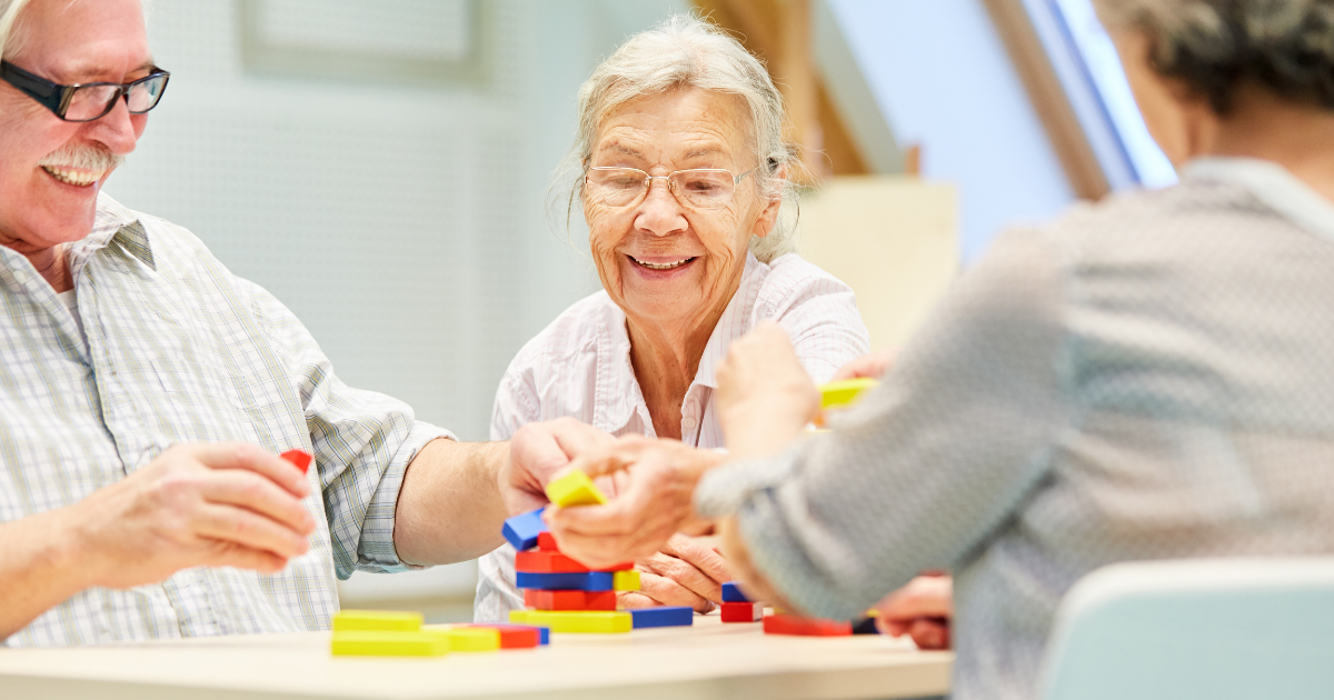 Three seniors sit together at a table participating in a colorful block-building activity.